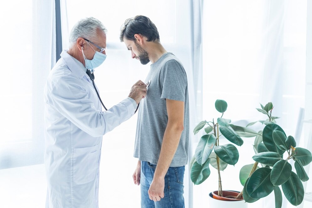 A healthcare professional in a white coat uses a stethoscope to examine a male patient in a medical setting, emphasizing medical care and professional healthcare.